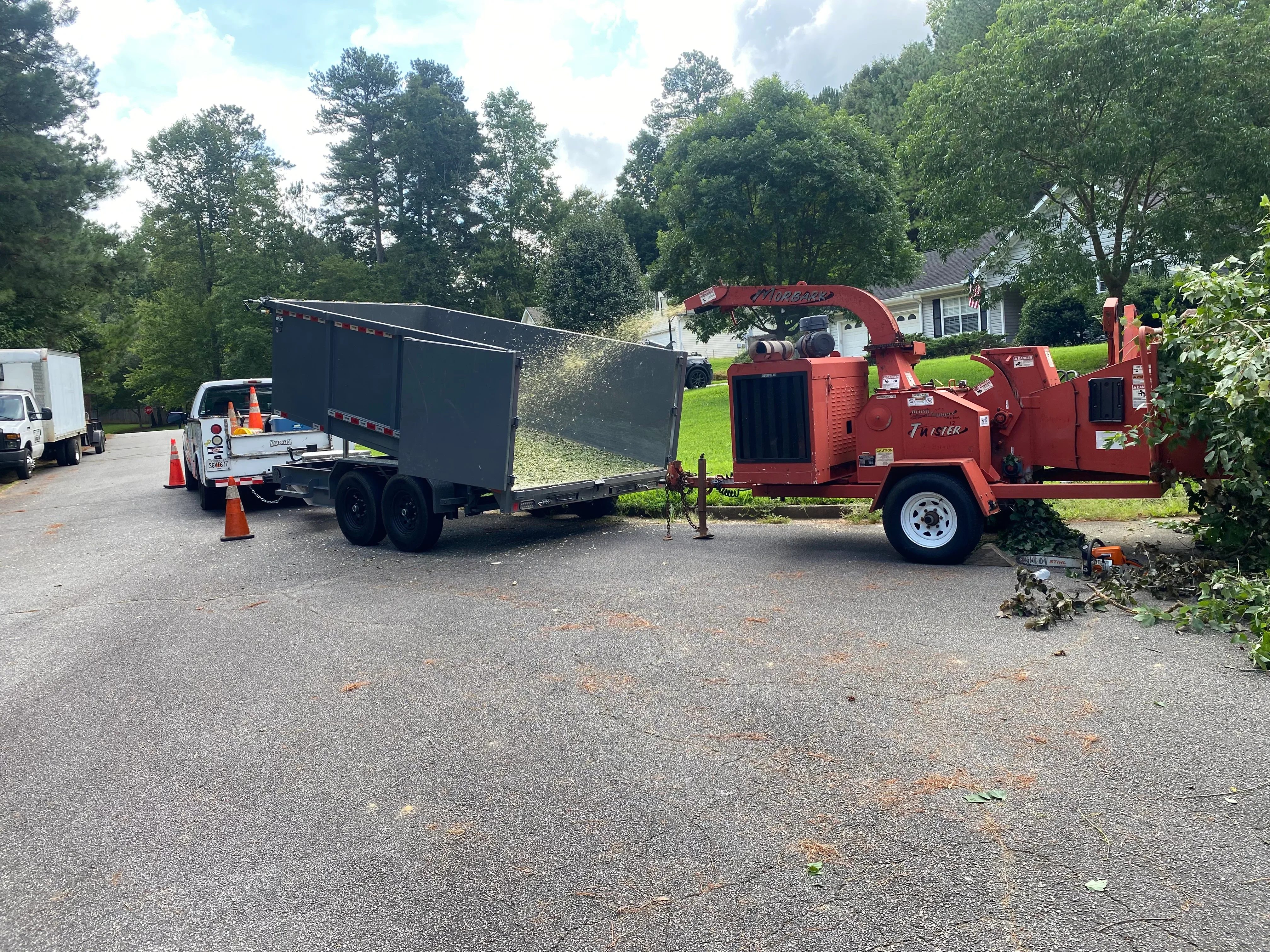 Red wood chipper processing tree branches with dump trailer and residential driveway setup