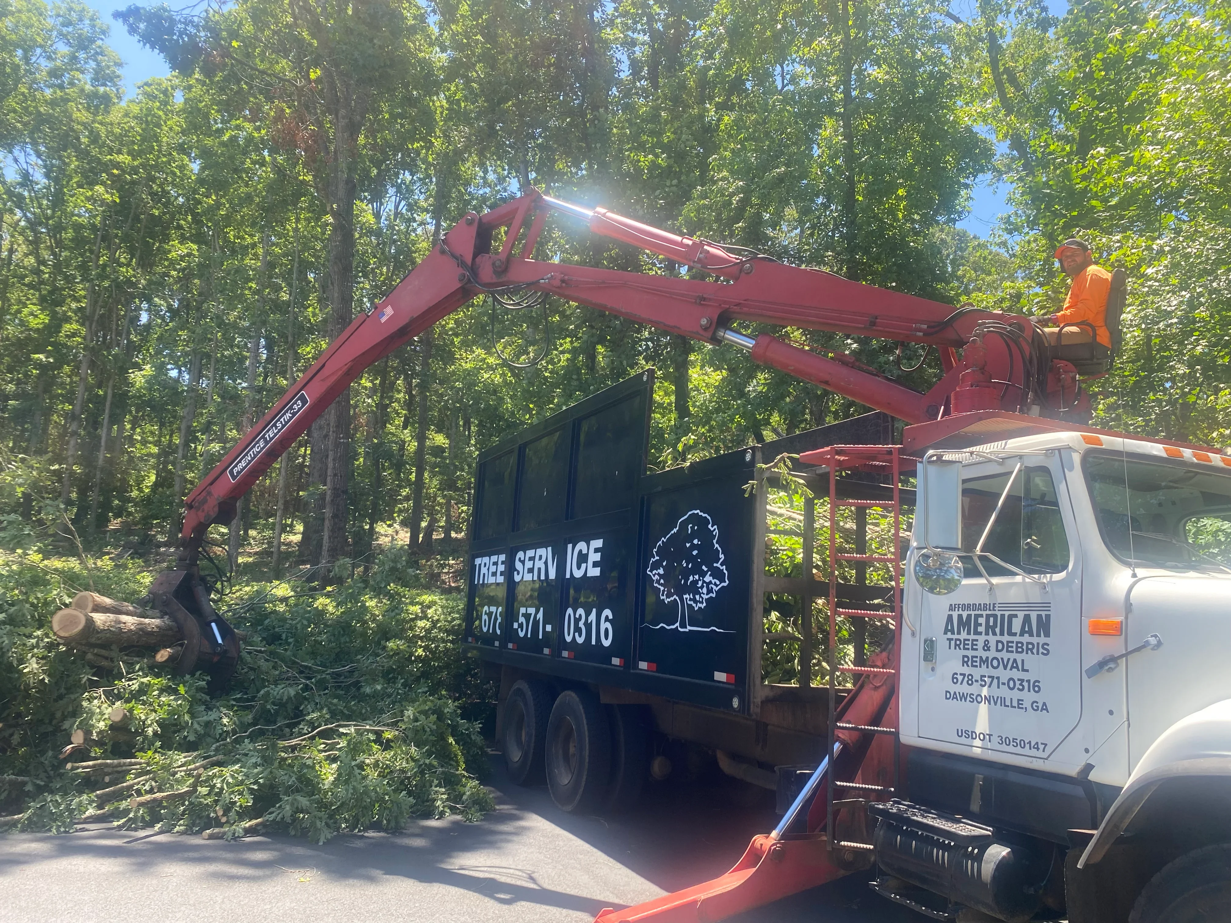 Red bucket truck with extended boom removing large tree, wood chips being loaded into truck bed