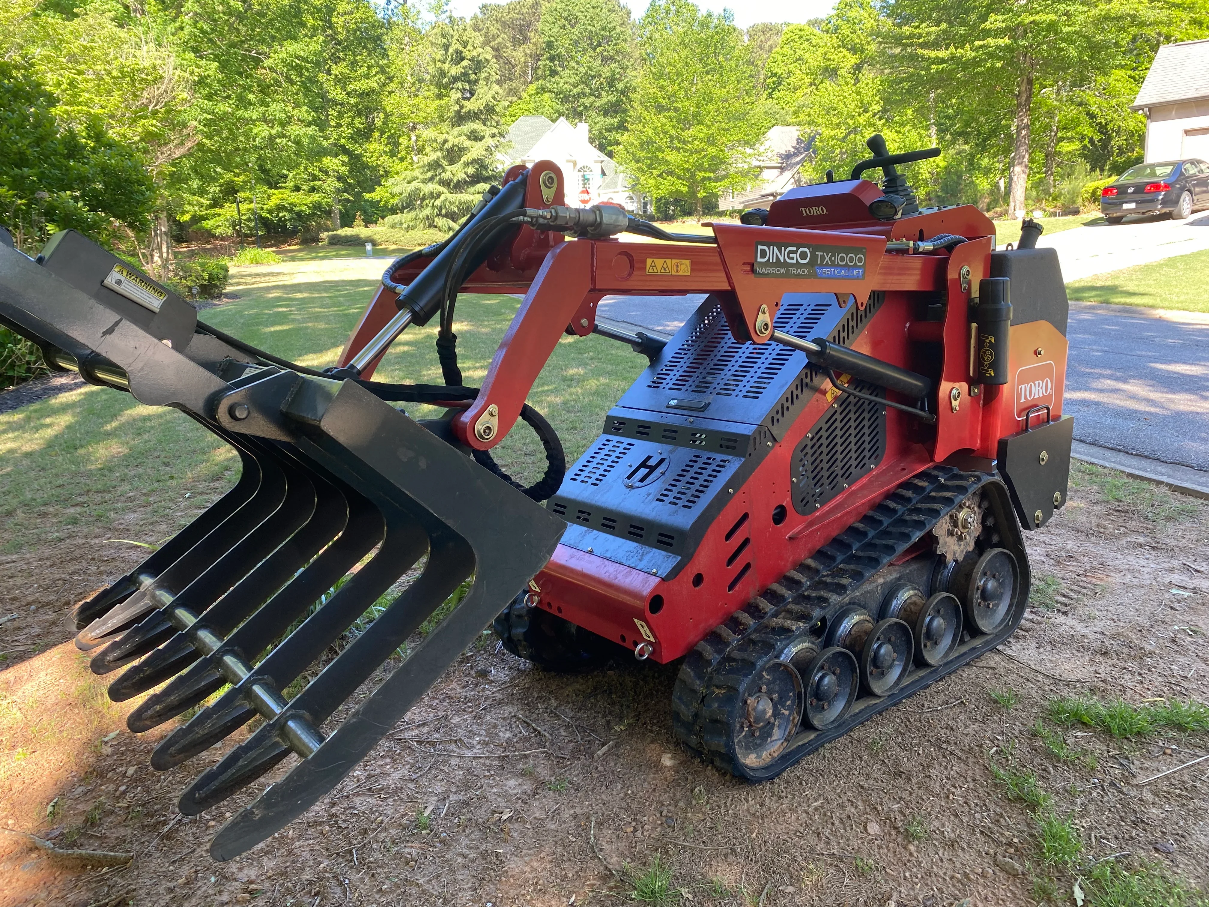 Red Toro Dingo TX1000 compact loader with black hydraulic grapple bucket attachment on residential driveway