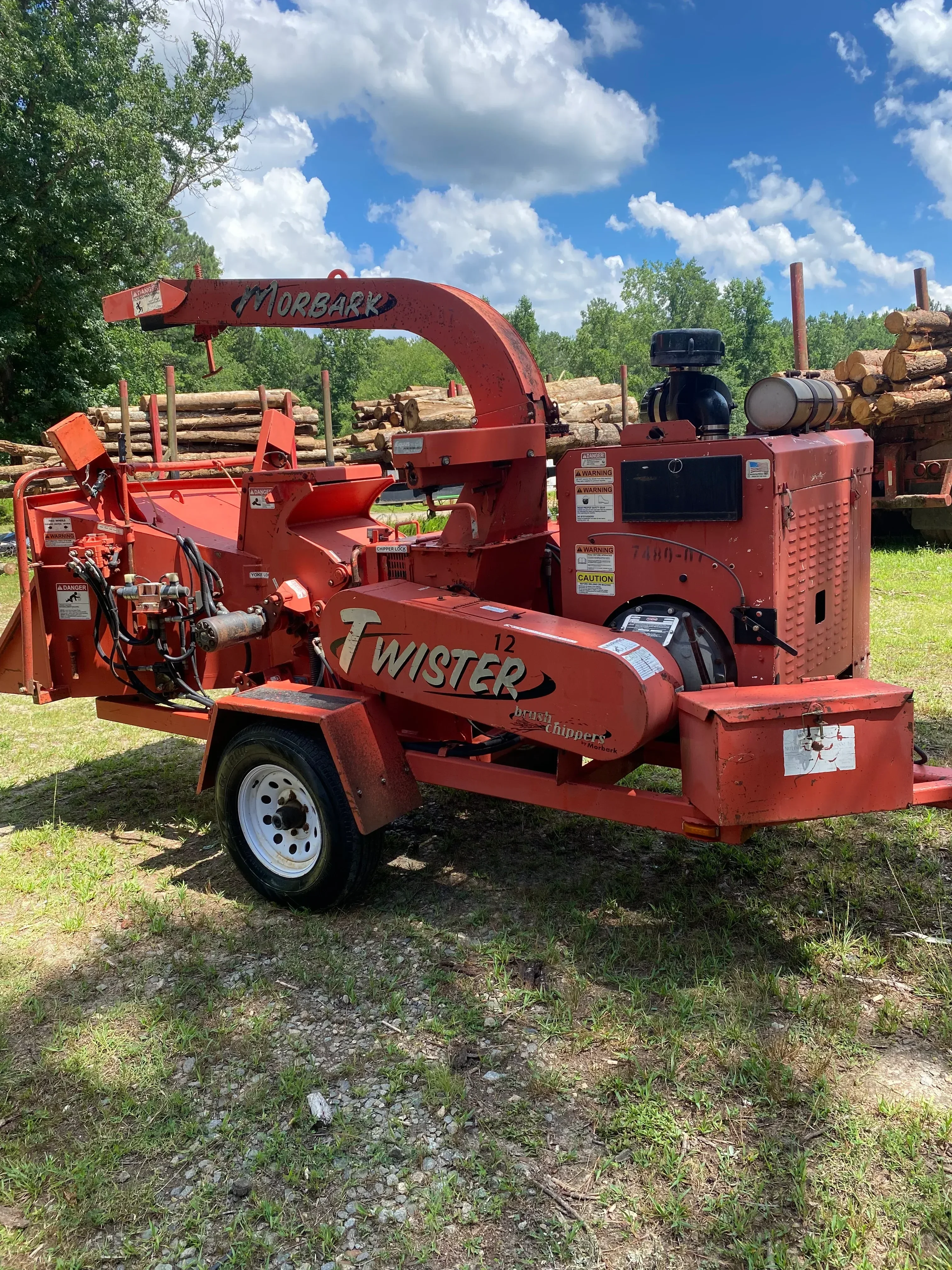 Red wood chipper with auger feed system processing tree branches and logs