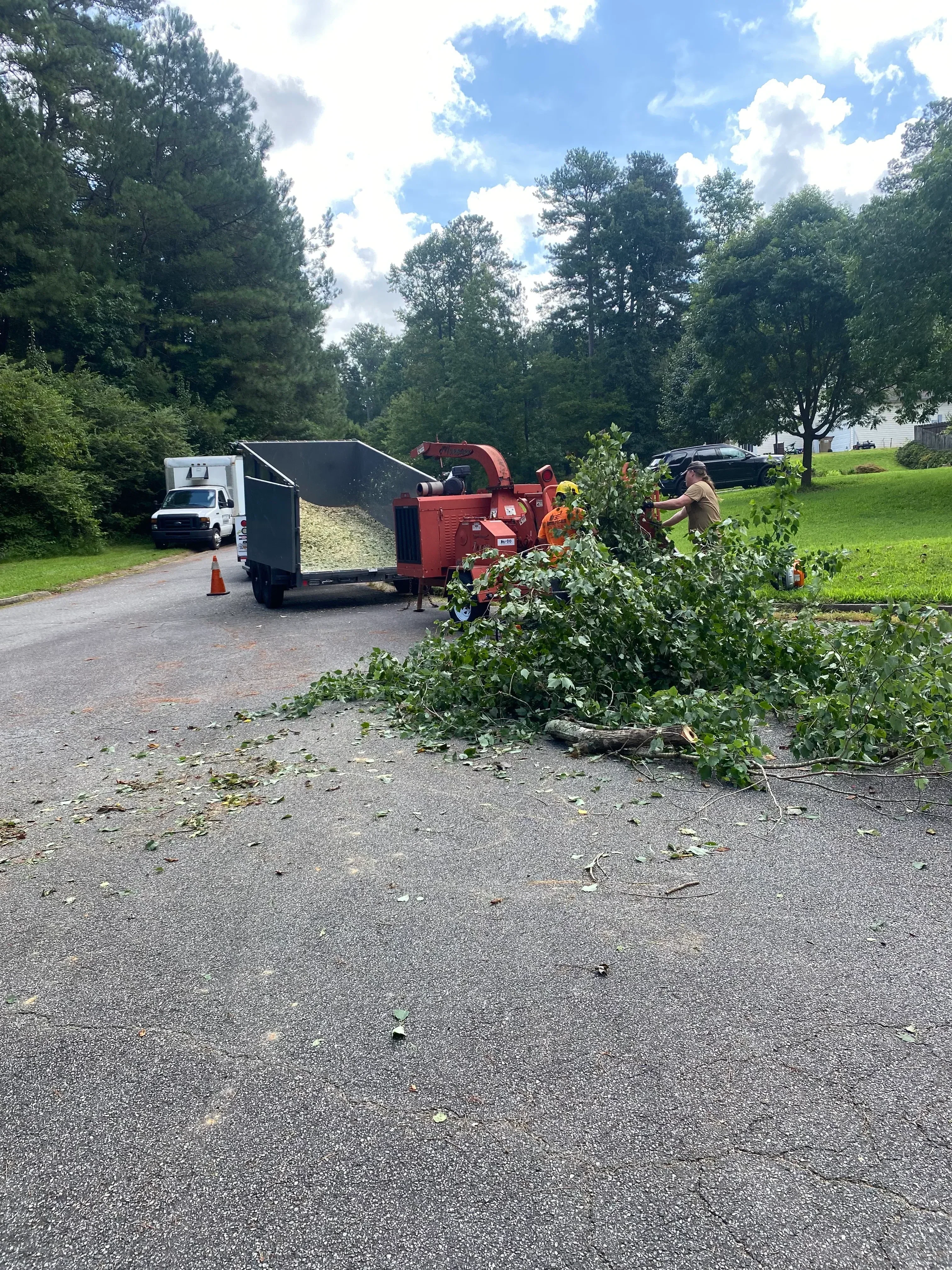 Wood chipper truck processing tree debris on residential driveway with crew operating equipment