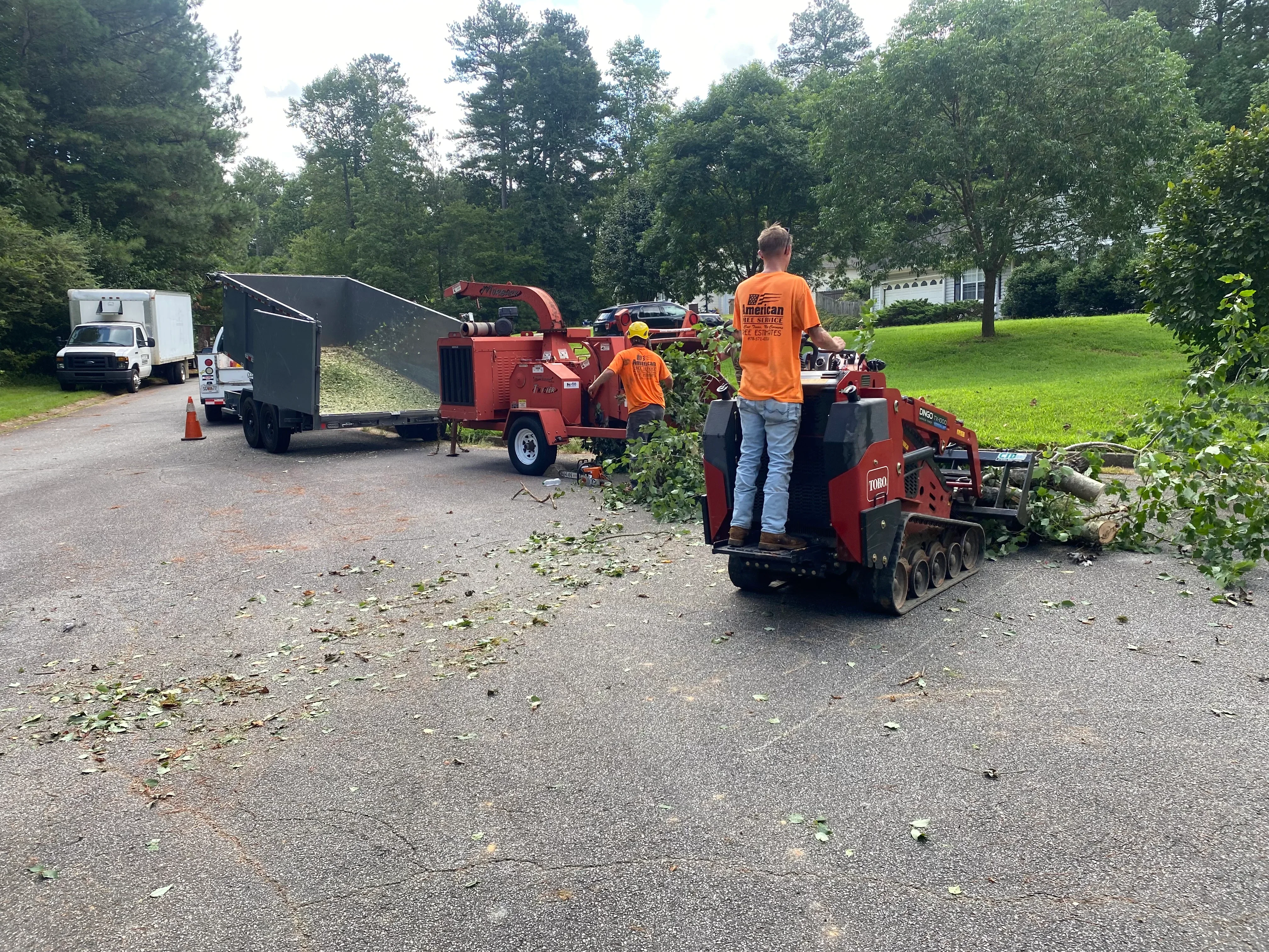 Wood chipper and crew processing tree branches with collection trailer on residential driveway