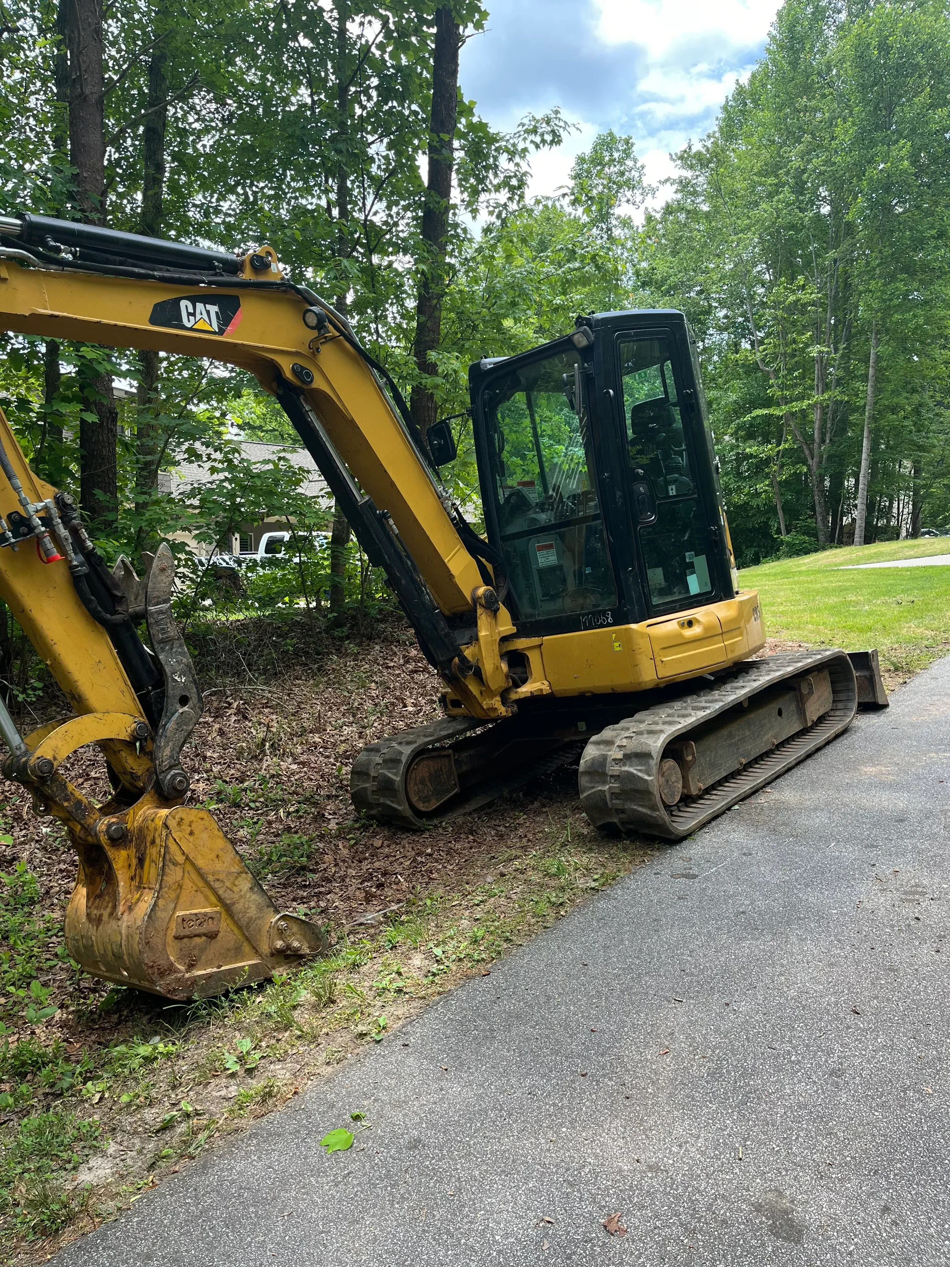 Yellow tracked excavator with hydraulic boom removing tree debris from residential yard
